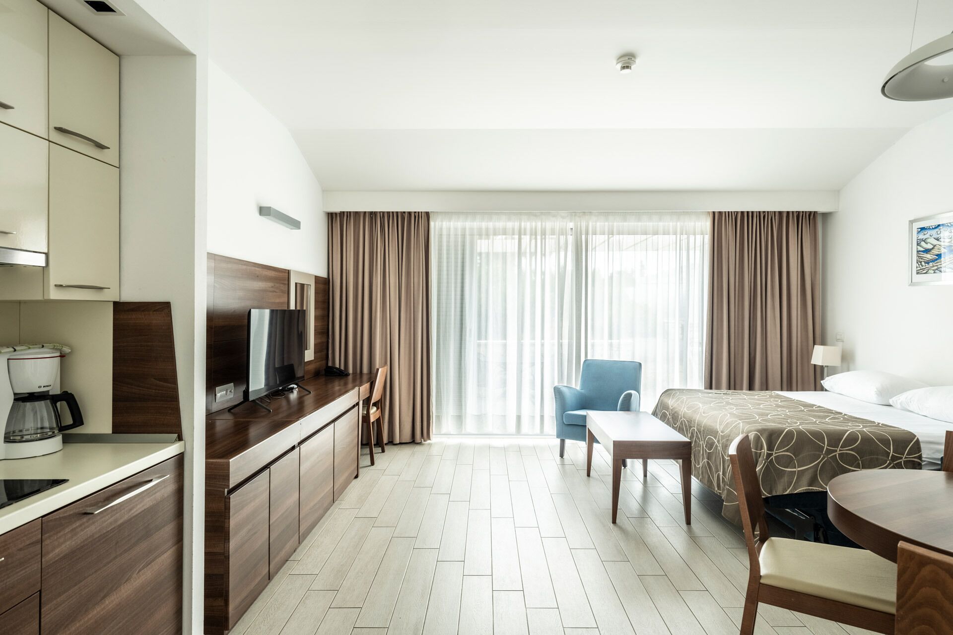 A hotel room with a bed, a desk with a TV, a chair, and a coffee maker.
