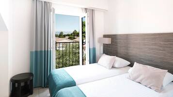 A hotel room with two beds, a view of a balcony, and a small trash bin.
