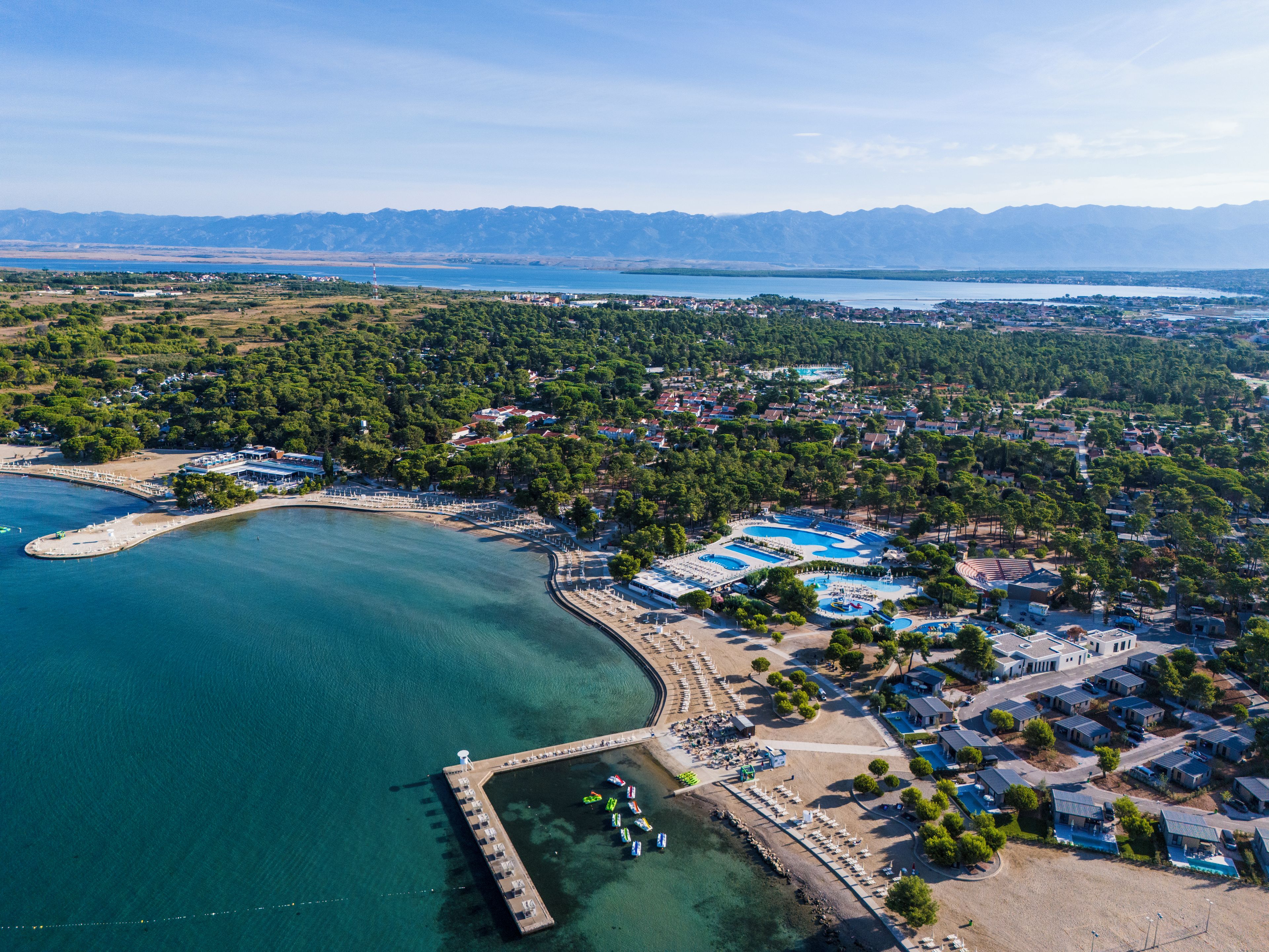 An aerial view of a coastal town with a marina, a beach, and residential areas.