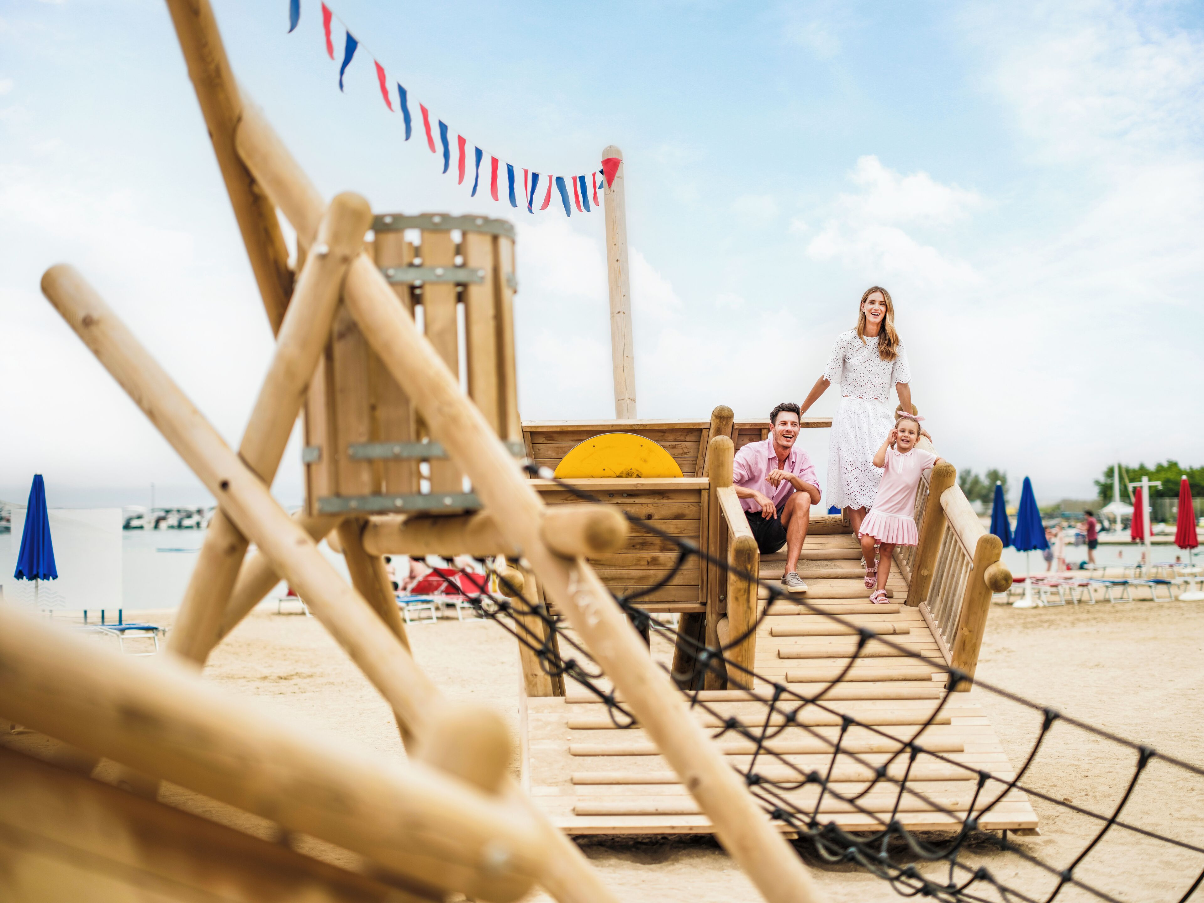 Eine Holzterrasse mit Seilgeländer, einem gelben Gegenstand und einer Person in einem weißen Kleid.