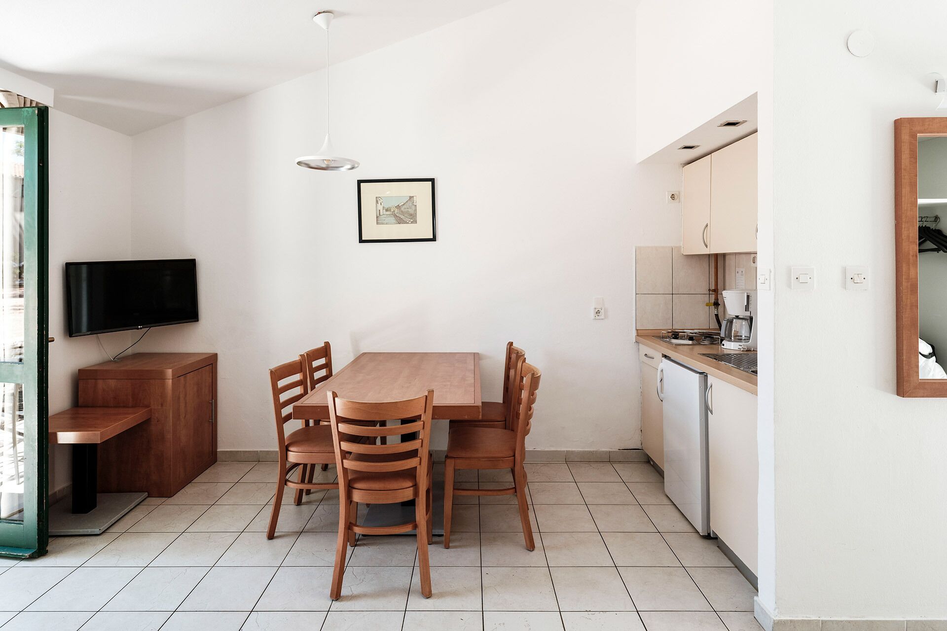 A compact living space with a dining table, chairs, a TV, and a kitchenette.