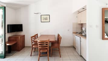 A compact living space with a dining table, chairs, a TV, and a kitchenette.