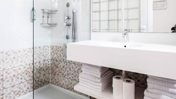 Een moderne badkamer met een glazen douchecabine, een witte wastafel en een betegelde douche.