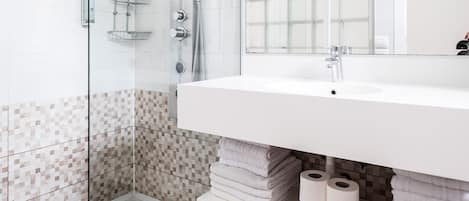 A modern bathroom with a glass shower enclosure, a white sink, and a tiled shower area.
