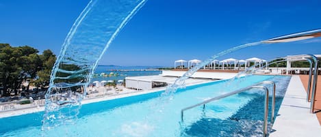 A pool with clear blue water, a metal railing, and umbrellas in the background.