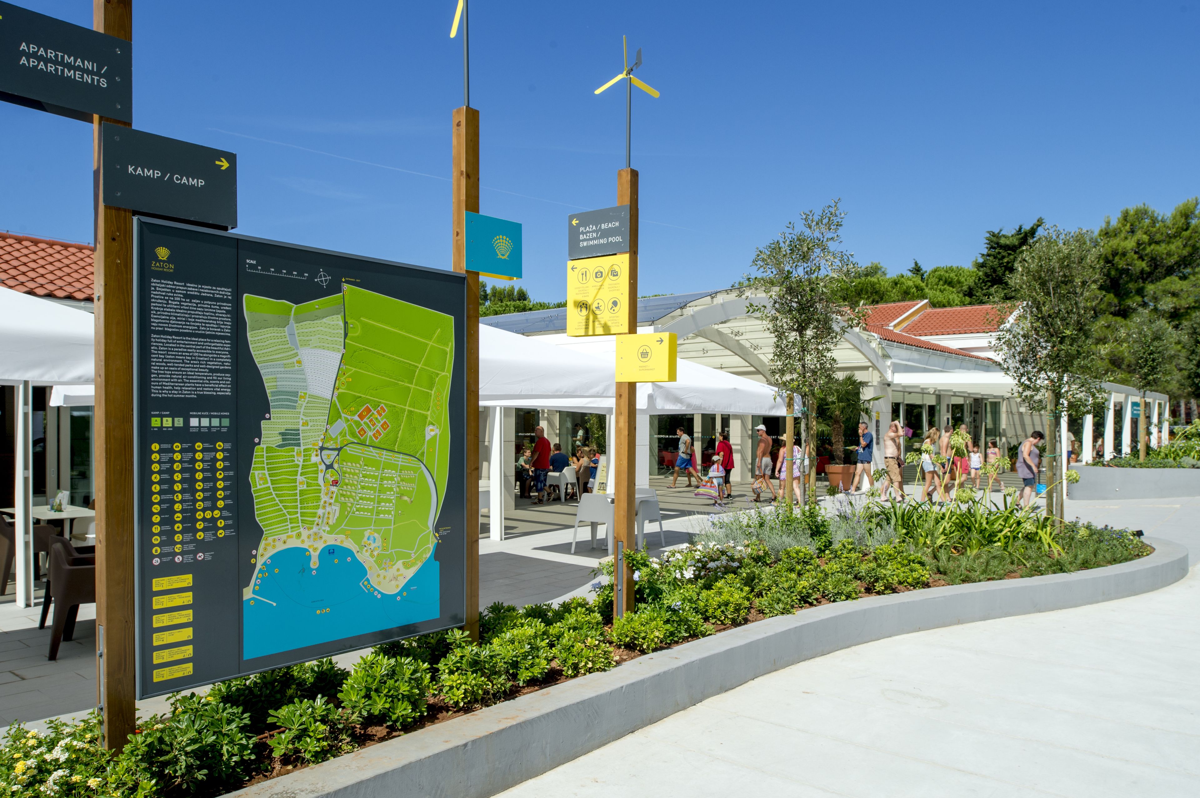 A map and directional signs at a resort, indicating amenities like apartments, a camp, and a beach.