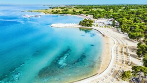 A coastal resort with a curved beach, clear blue waters, and a row of sun loungers along the shore. - Zaton Holiday Resort Apartments (Nin)