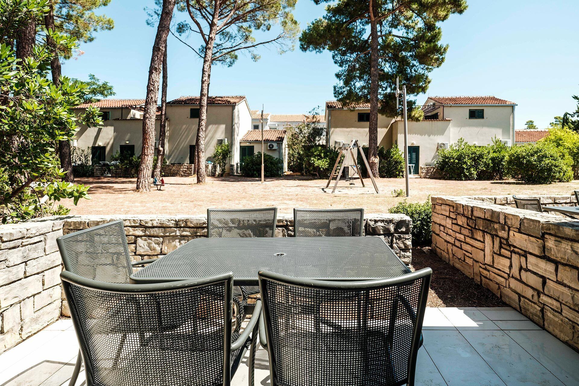 Un espace extérieur aménagé avec une table et des chaises, entouré de murs en pierre et d’arbres.