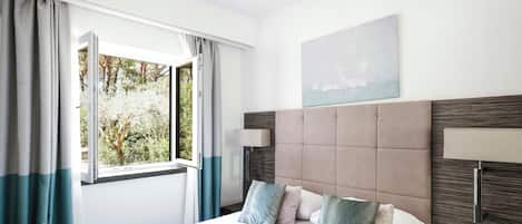 A hotel room with a bed, a nightstand, a window with curtains, and a painting on the wall.