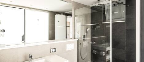 Un baño moderno con ducha de vidrio, un lavabo blanco y un espejo grande.