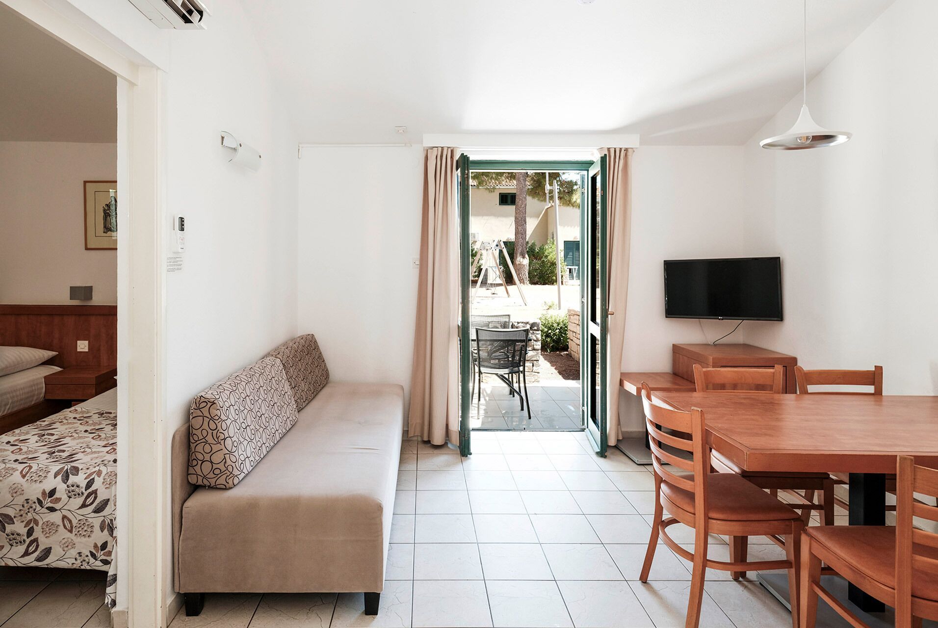 Una habitación con cama, sofá, mesa de comedor con sillas, televisor y vistas al exterior.