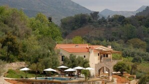 Una vila amb piscina, envoltada d'arbres i muntanyes.