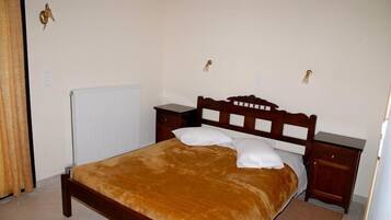 Quarto com cama de madeira, mesa de cabeceira, radiador e luminária fixada na parede.