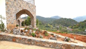 Edifici de pedra amb entrada arquejada i jardí paisatjistic amb roques i plantes.