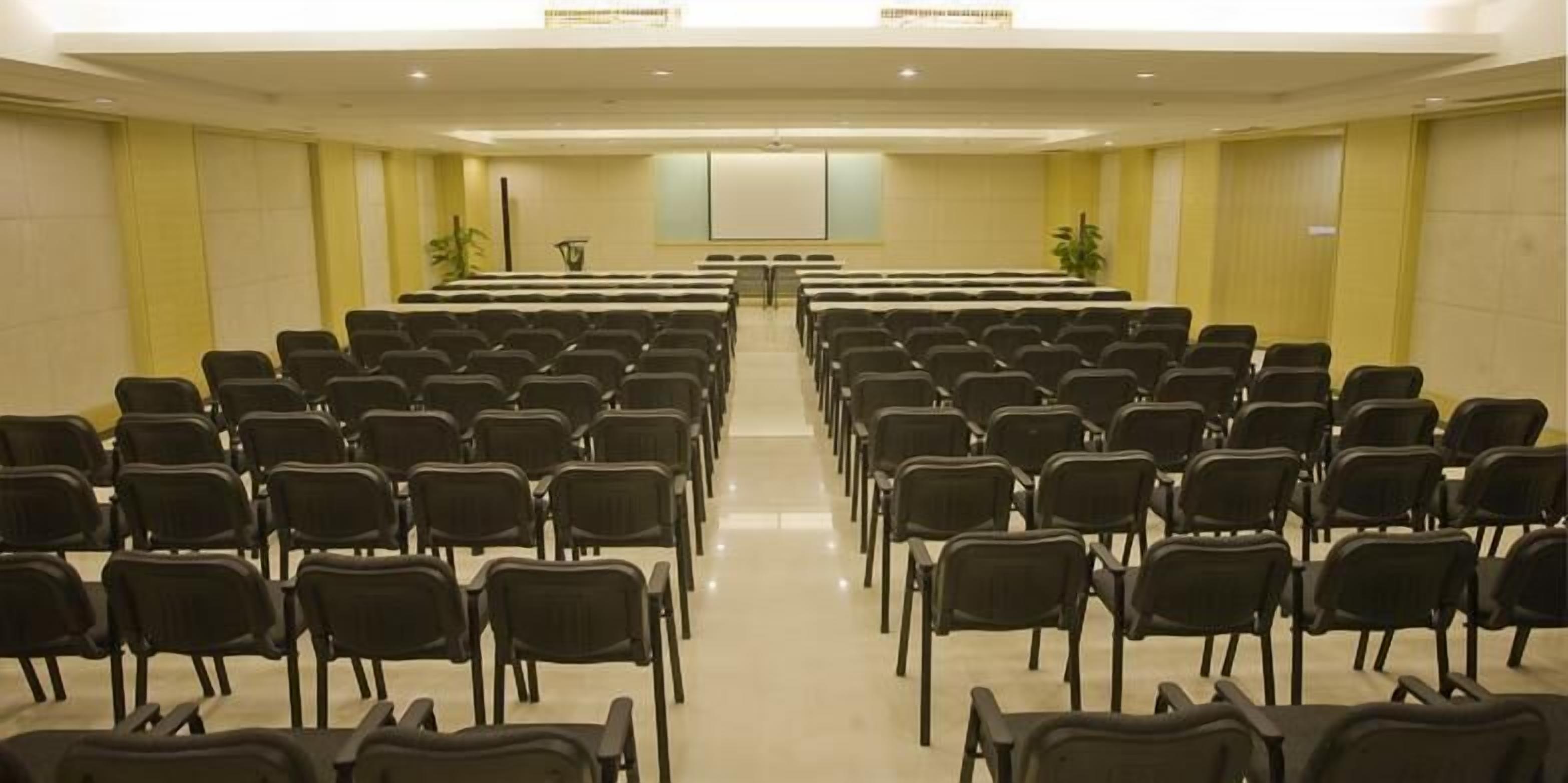Un salón de conferencias con filas de sillas negras orientadas hacia una pantalla de proyección.