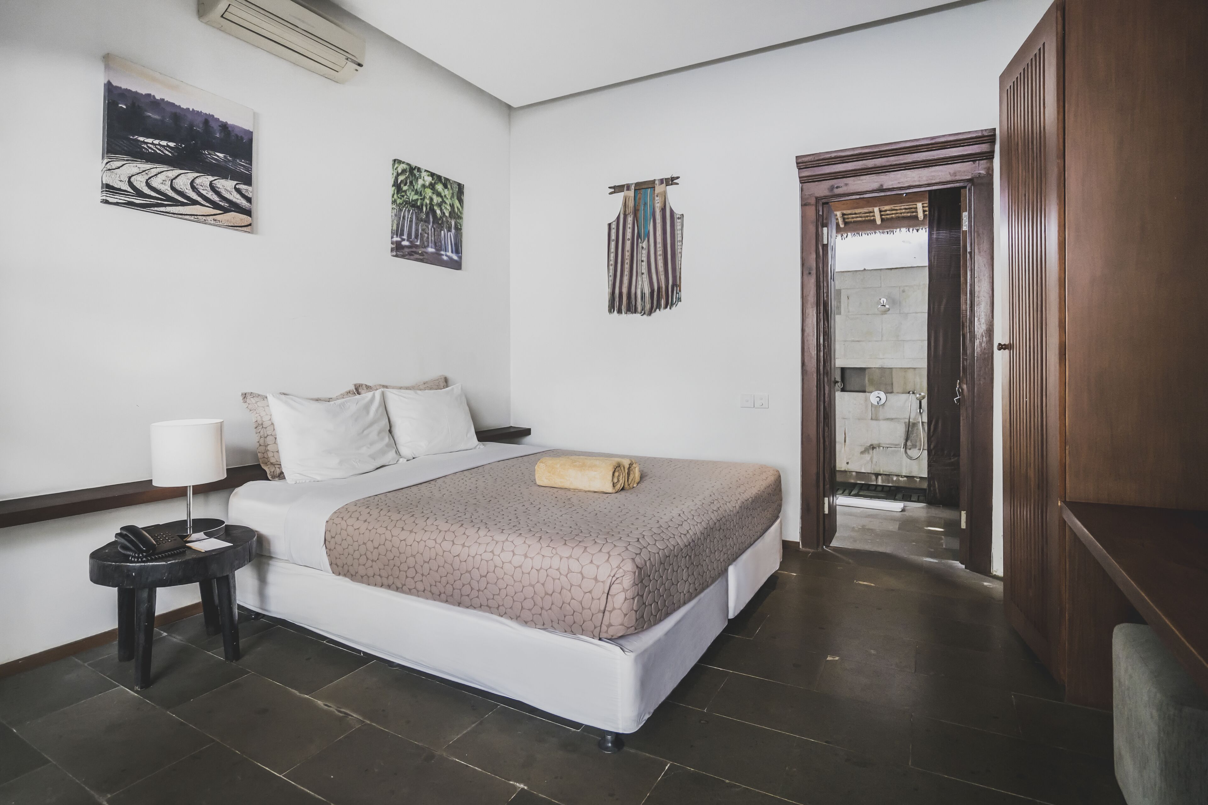A hotel room with a bed, a nightstand, a lamp, and artwork on the walls.