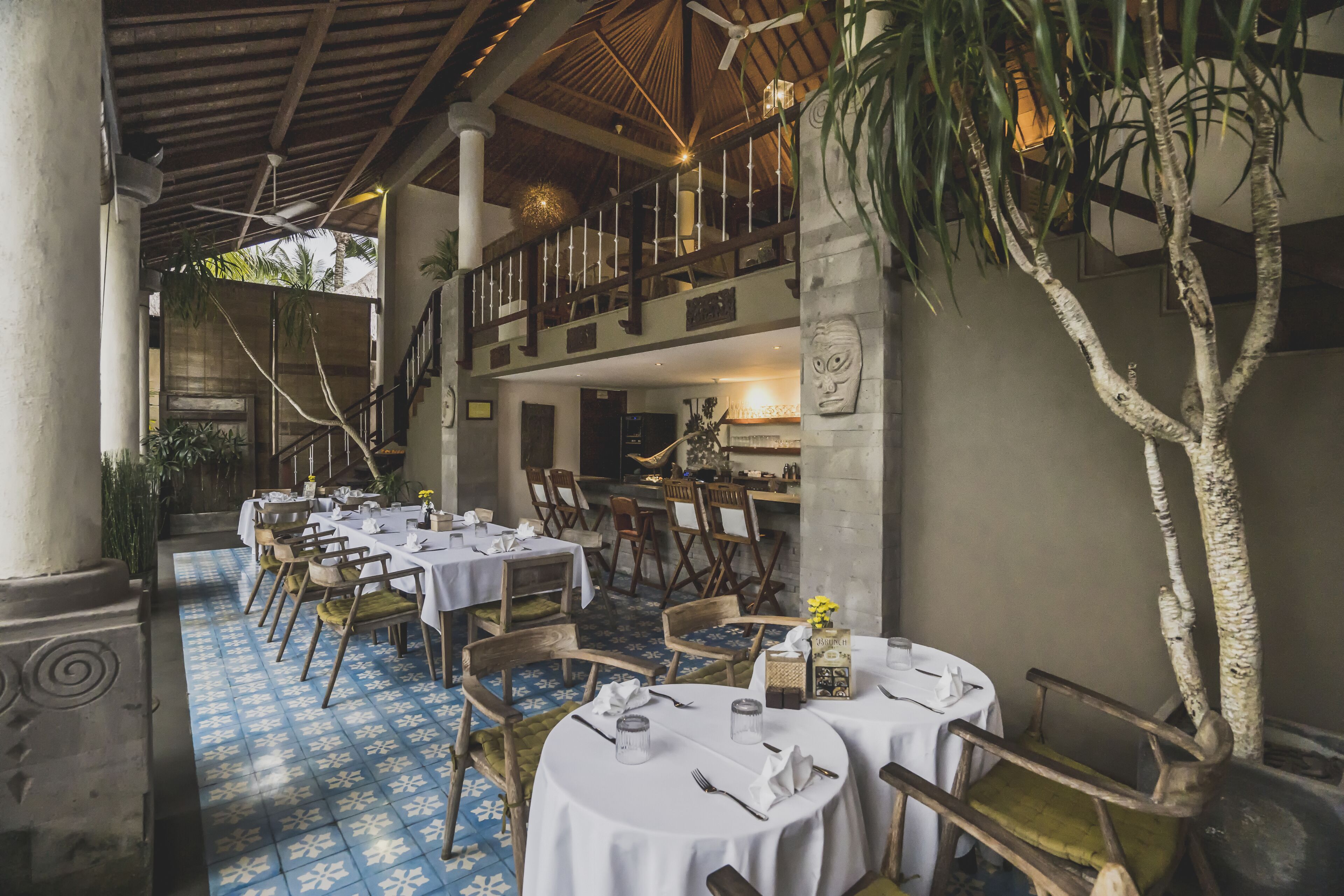 Un restaurante con mesas y sillas redondas, un suelo estampado en azul y un balcón con barandilla.