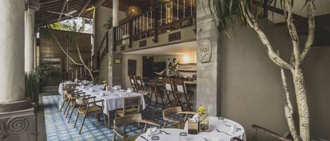 A restaurant with round tables and chairs, a blue patterned floor, and a balcony with a railing.