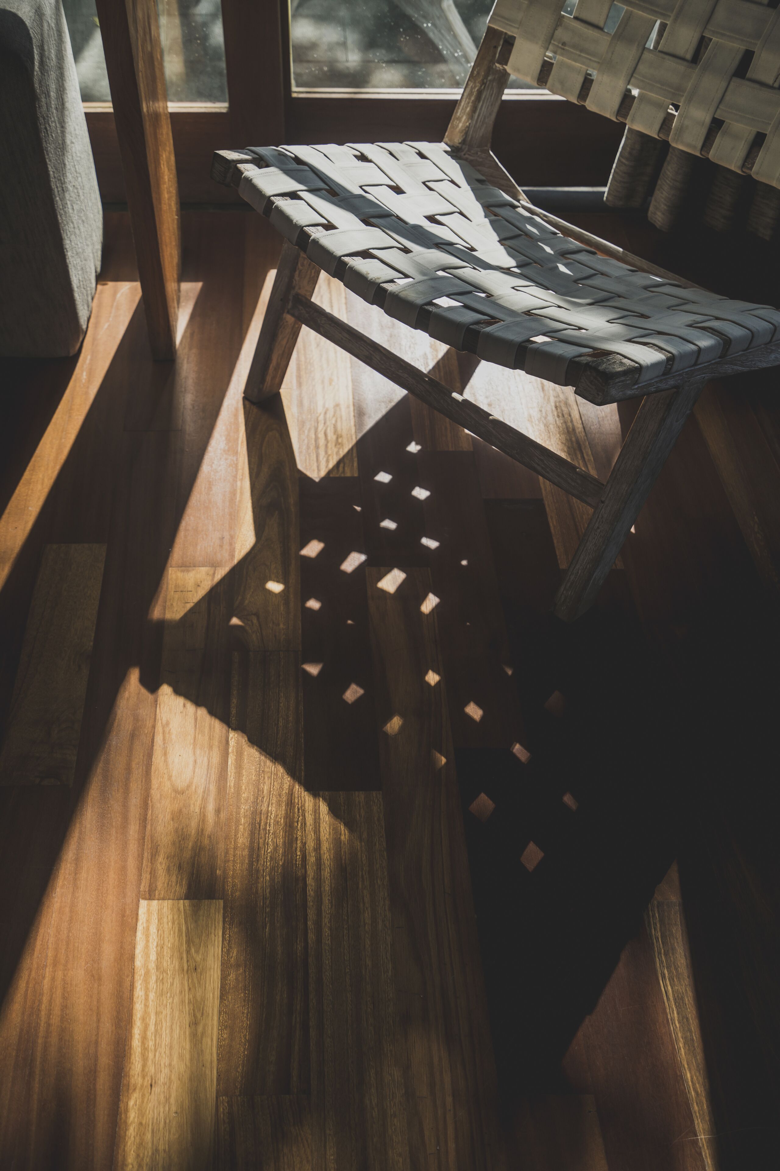 A wooden floor with a woven bench and a window casting light.