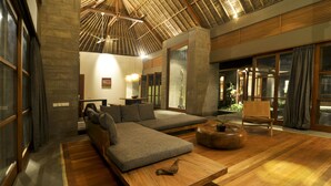 A modern living room with a sectional sofa, a wooden coffee table, and a large window with curtains. - Luwak Ubud Villa & Jungle Suite (Ubud)