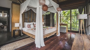 A four-poster bed with a canopy, a wooden floor, a nightstand with a lamp, and a view of greenery outside. - Luwak Ubud Villa & Jungle Suite (Ubud)