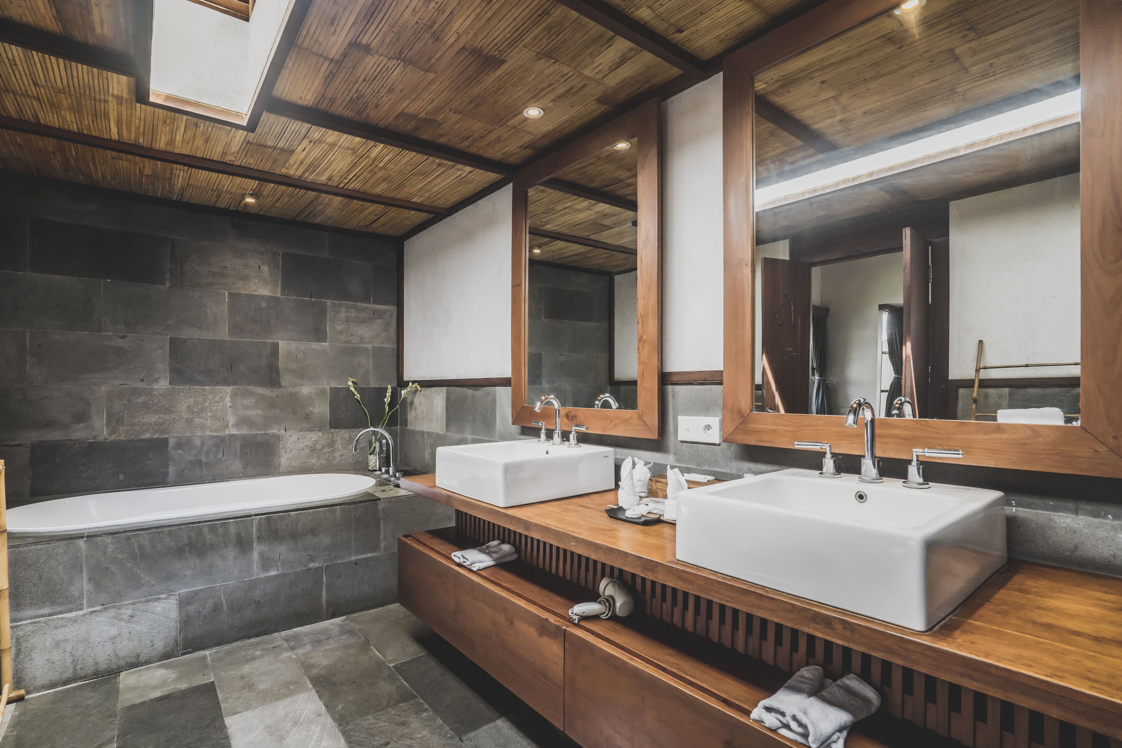 A modern bathroom with a wooden vanity, two sinks, a bathtub, and a large mirror.