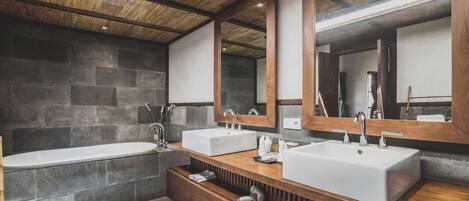 A modern bathroom with a wooden vanity, two sinks, a bathtub, and a large mirror.