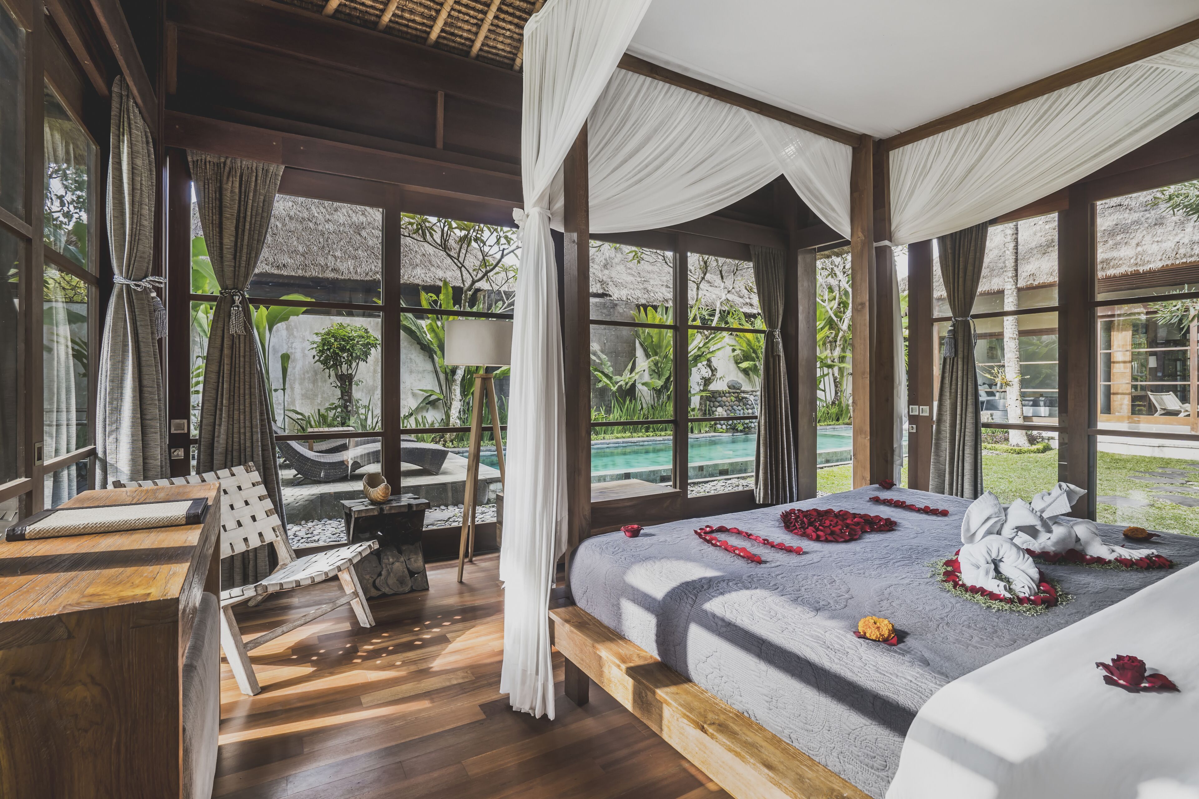 Ein geräumiges Schlafzimmer mit einem großen Bett, Holzmöbeln und Blick auf einen Swimmingpool.