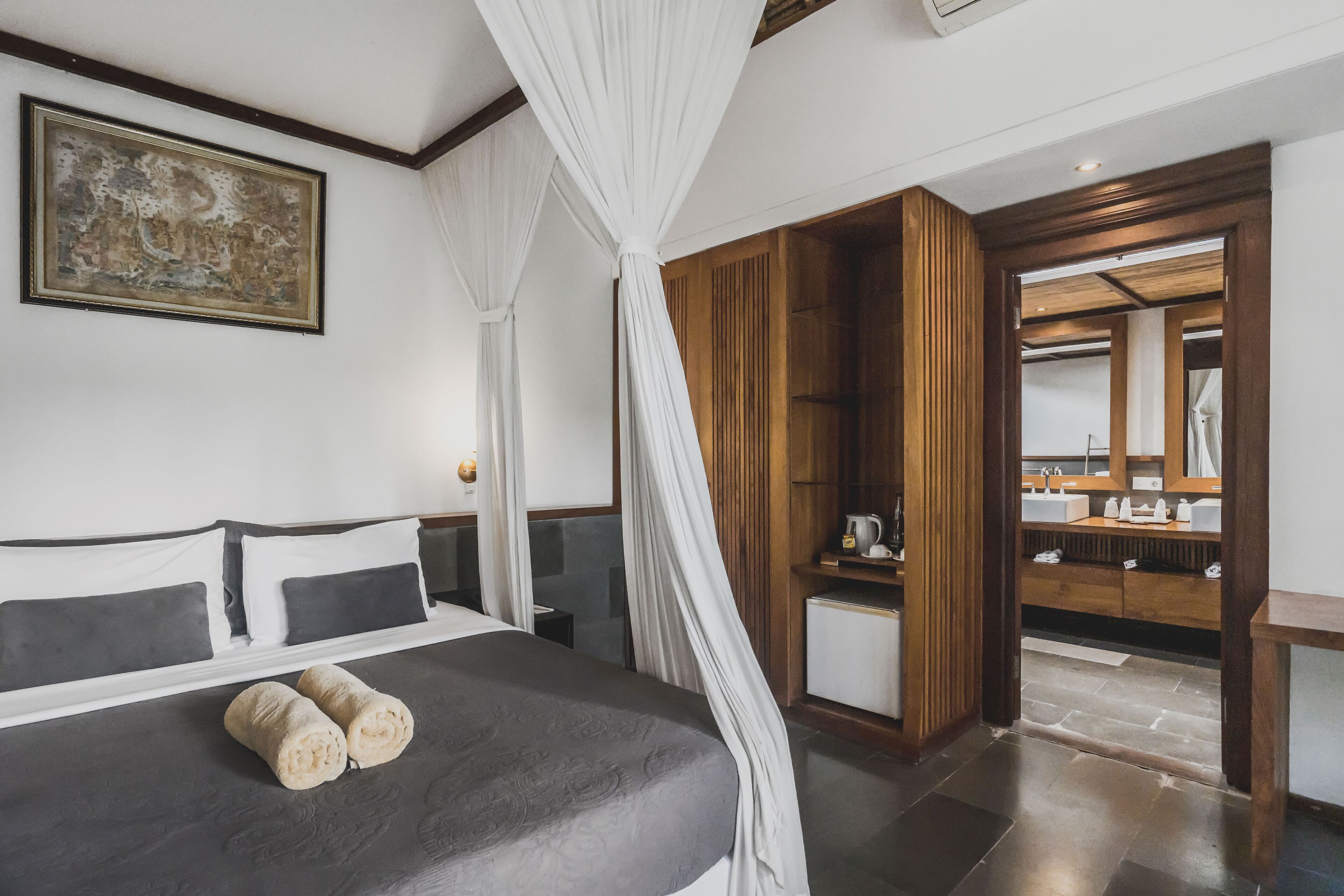 Un dormitorio con cama, mesita de noche, escritorio, silla, armario y baño con lavabo y espejo.