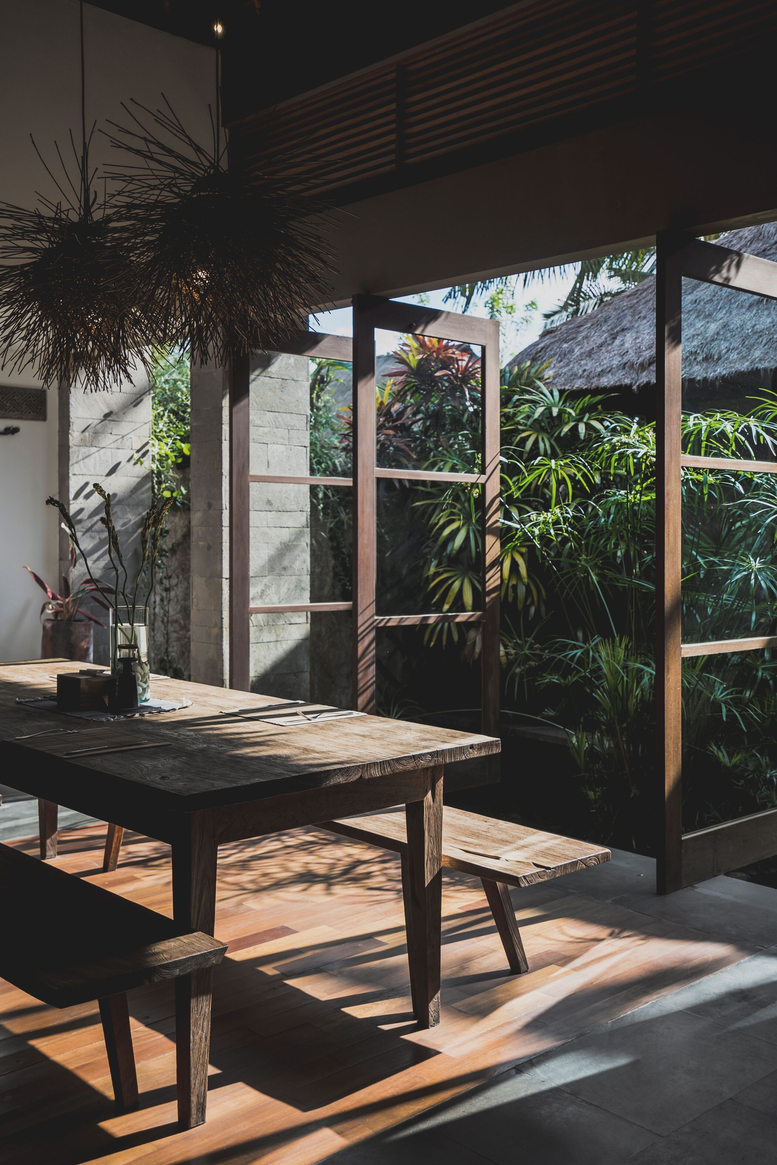 A wooden dining table with benches, large windows, and a hanging plant.