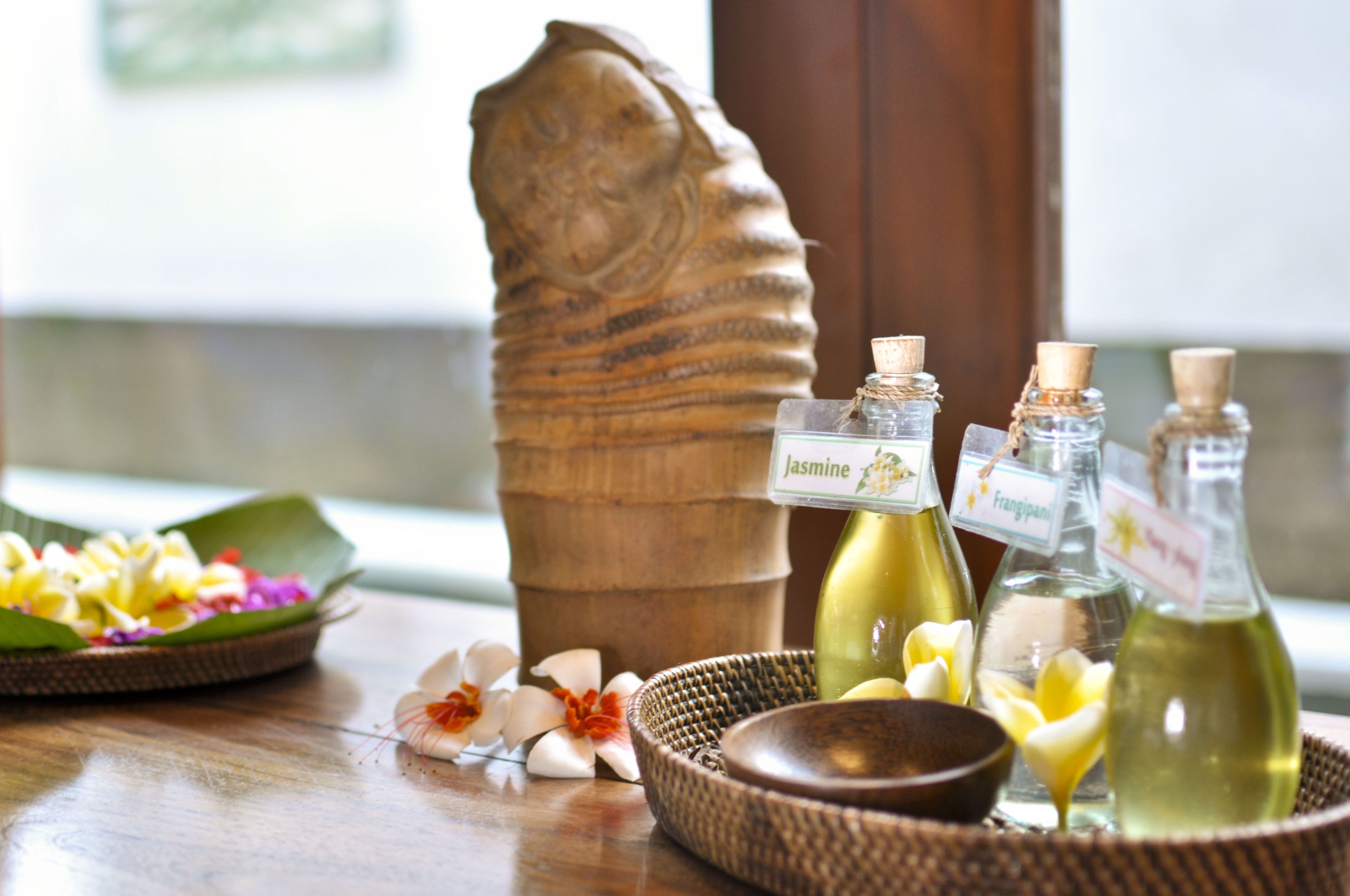 Una escultura de madera, un cuenco con flores y tres botellas etiquetadas sobre una mesa.