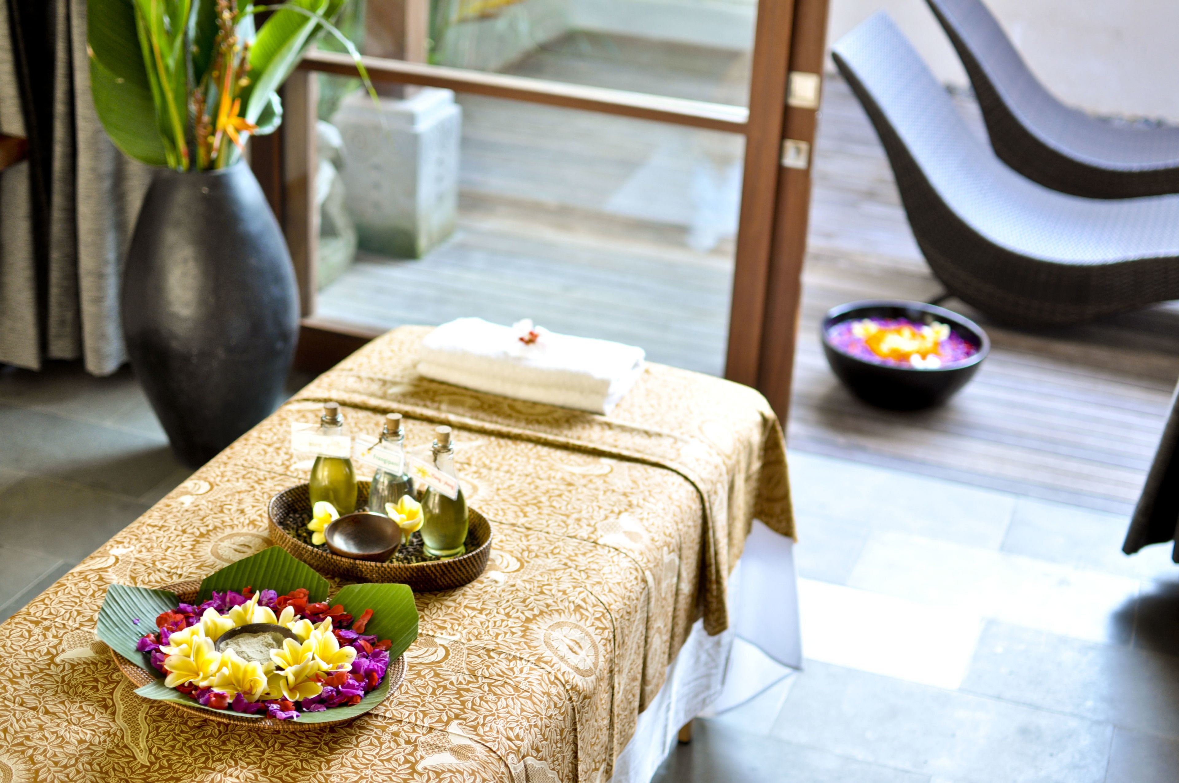 A table with a towel, a bowl of flowers, and a small dish with a white substance, likely for a spa treatment.