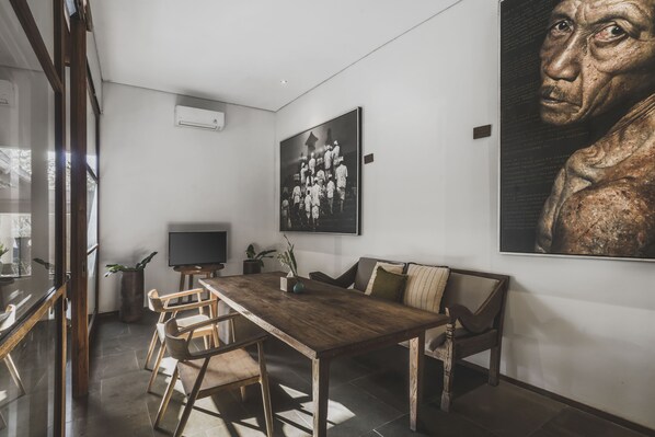 A modern dining area with a wooden table and chairs, a television, and a large framed artwork on the wall.