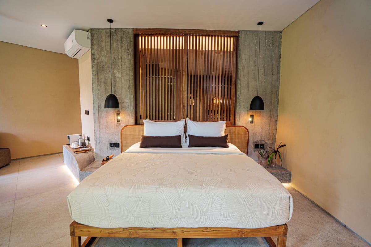 A modern bedroom with a large bed, wooden headboard, two bedside tables with lamps, and a decorative wall panel.