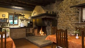 Un comedor rústico con chimenea de piedra, sillas de madera y una mesa dispuesta para dos.