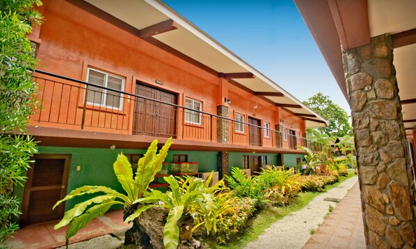 A multi-story building with balconies, surrounded by lush greenery and a stone wall. - Flushing Meadows Resort and Playground (Dauis)