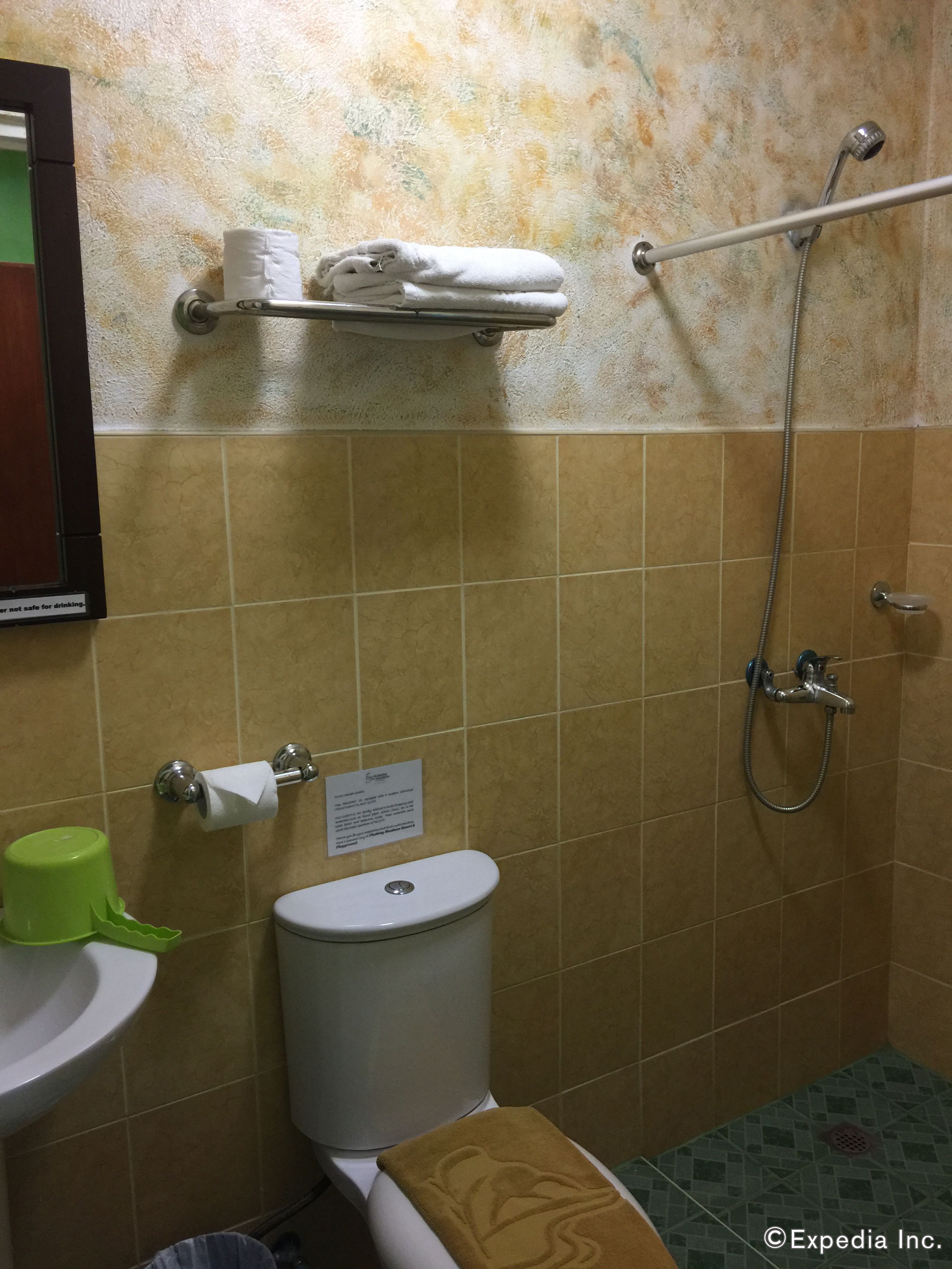 Et badeværelse med toilet, håndvask og brusebad. Der er en håndklædestang med håndklæder og en toiletpapirholder.