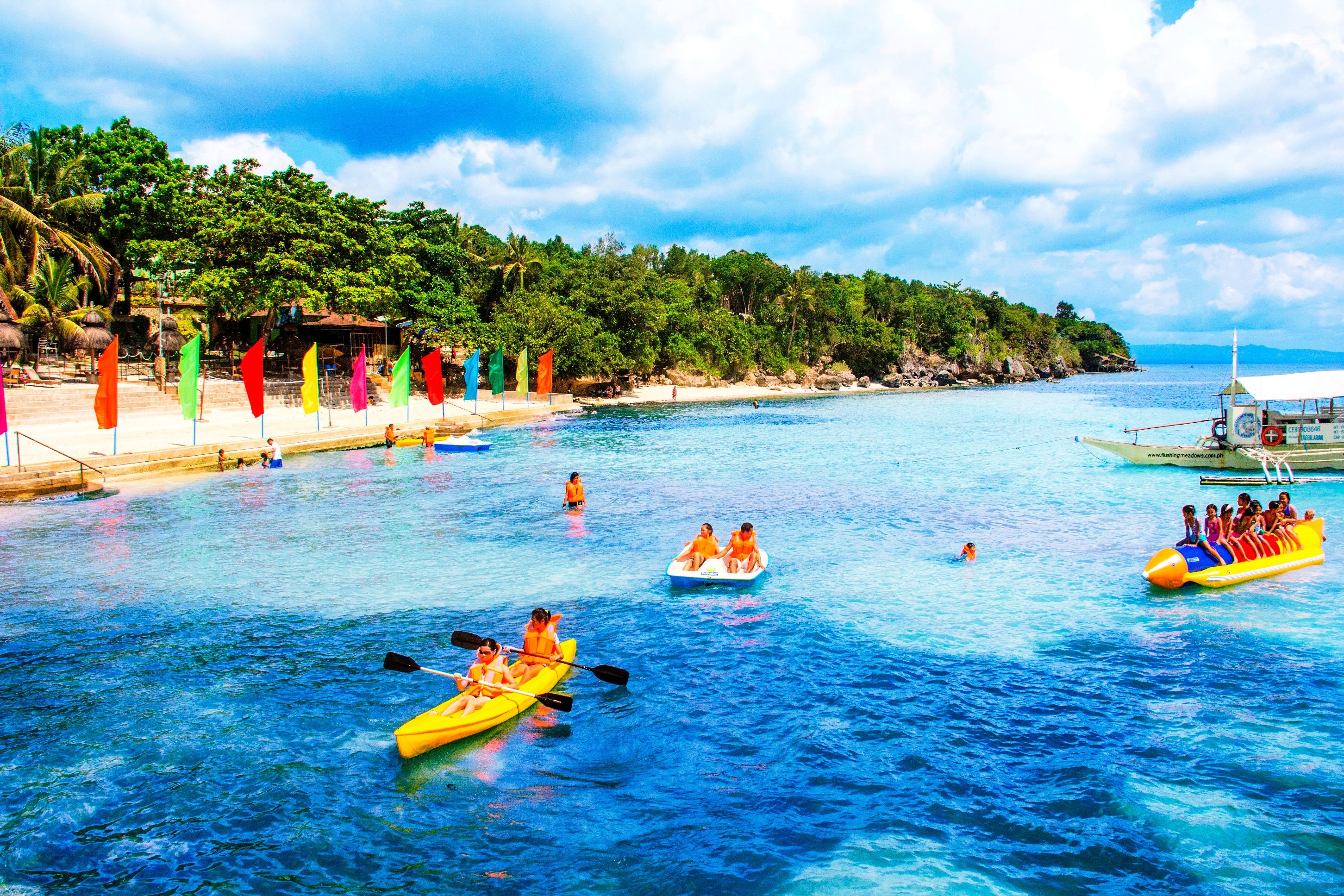 A beach with clear blue water, kayaks, and a boat with people.