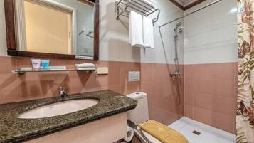 A bathroom with a granite sink, toilet, and shower. There is a towel rack with towels and a glass shelf with toiletries.