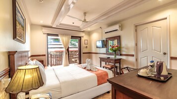 Una habitación de hotel con cama, mesita de noche, lámpara, escritorio, silla, televisor y un balcón con vistas.