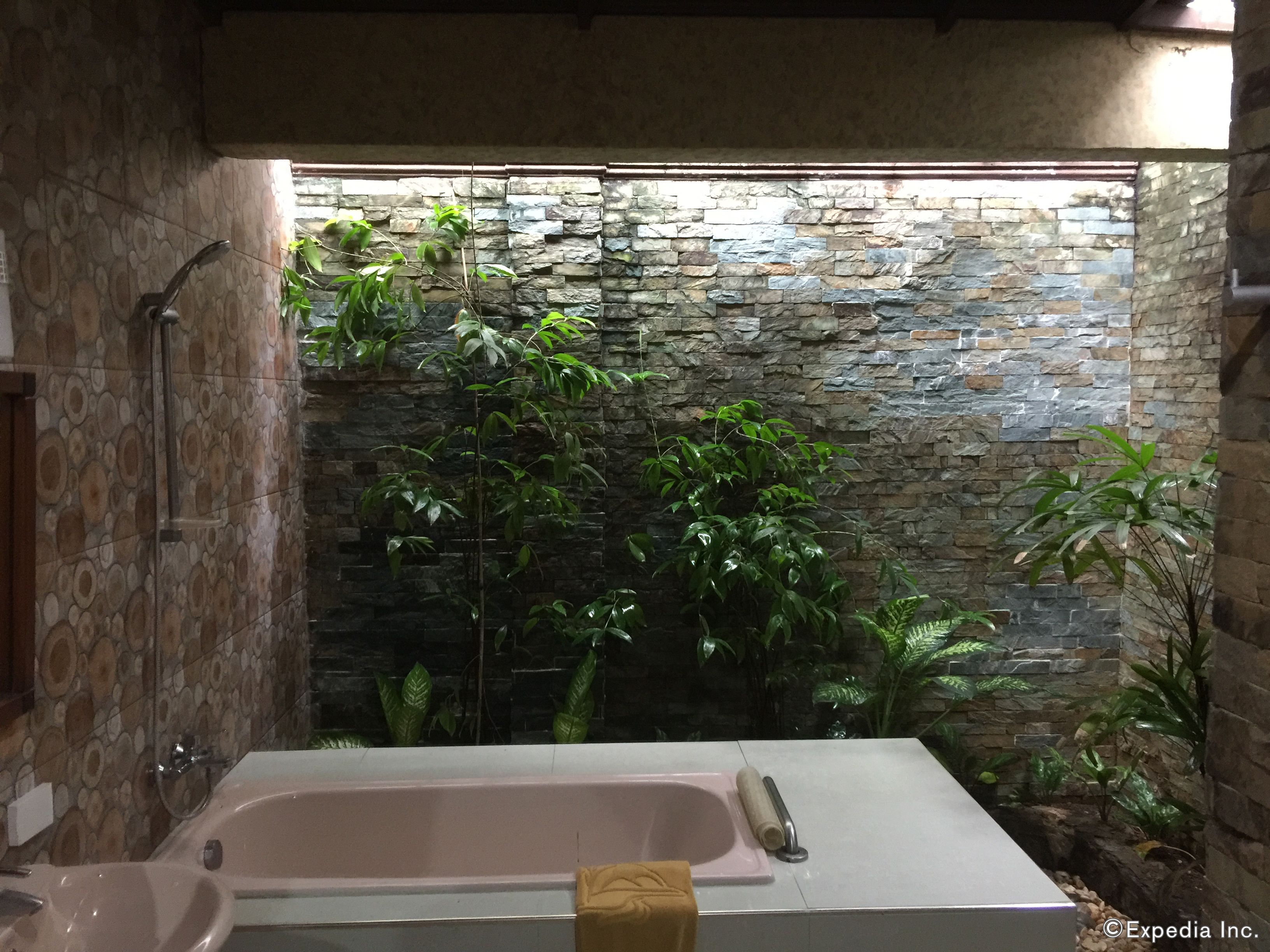 A bathroom with a bathtub, a shower, and a stone wall with plants.