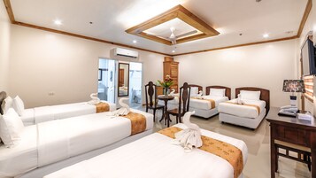 A hotel room with three single beds, a wooden ceiling, a desk with a lamp, and a mirror.