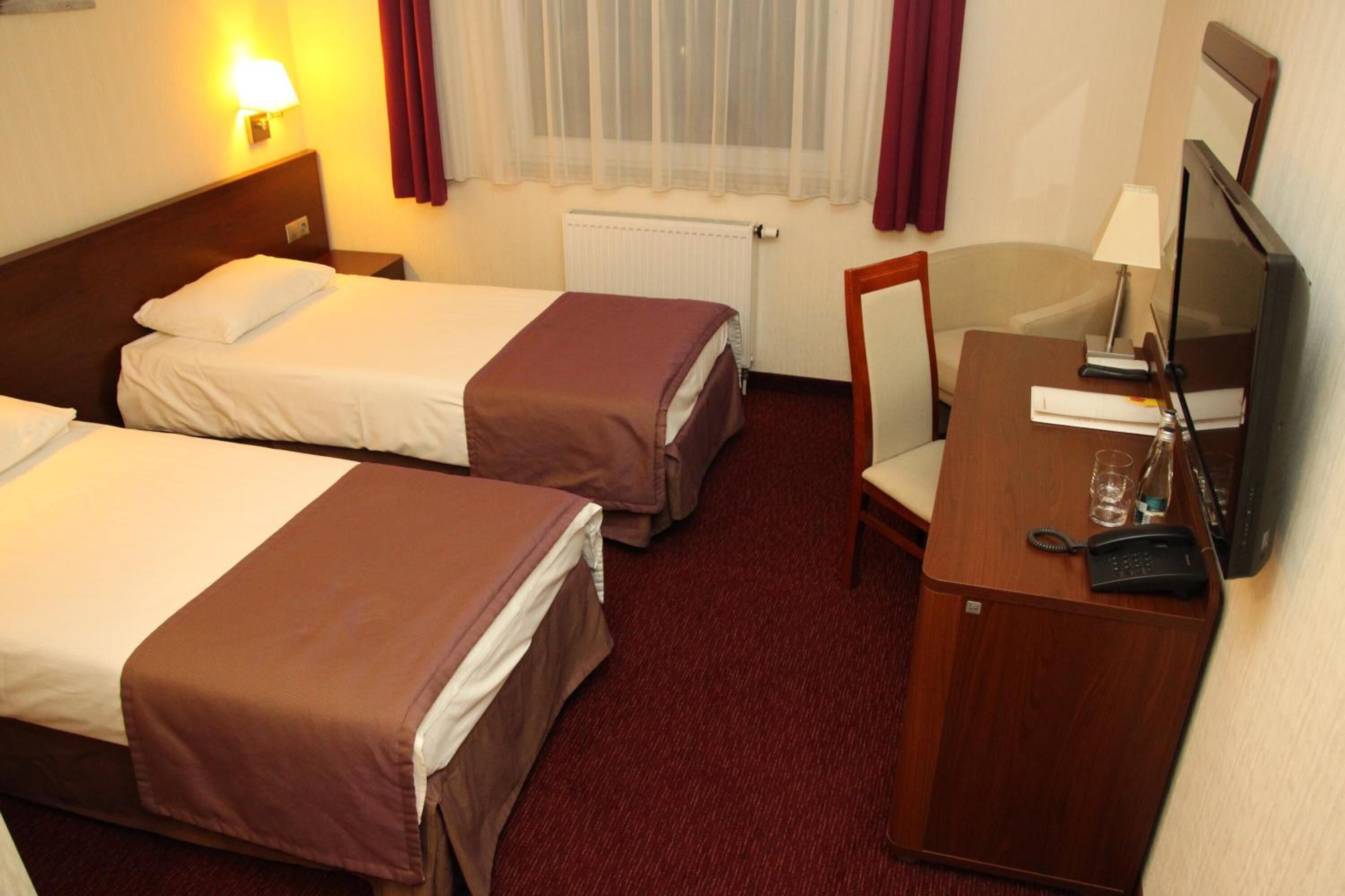 Una habitación de hotel con dos camas individuales, un escritorio con silla, televisor y teléfono.
