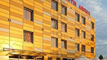 A hotel with a yellow facade, multiple windows, and a sign reading "HOTEL ARENA".