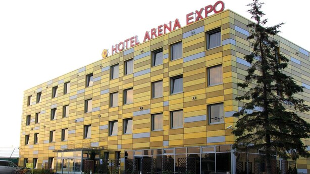 Un hôtel à la façade jaune, doté de nombreuses fenêtres et d’une enseigne indiquant « HÔTEL ARENA EXPO ».