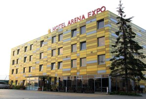 Un hôtel à la façade jaune, doté de nombreuses fenêtres et d’une enseigne indiquant « HÔTEL ARENA EXPO ».