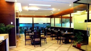 A modern indoor space with multiple tables and chairs, large windows, and a tiled floor. - Jht Hotels (New Delhi)
