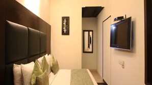 A modern hotel room with a large bed, a flat-screen TV mounted on the wall, and a small window. - Jht Hotels (New Delhi)