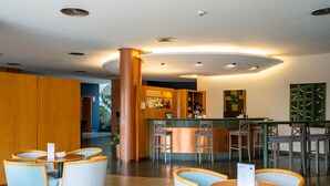 Un área de bar moderna con mesas redondas y taburetes, un pilar central y una barra con menú.