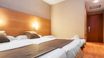 A hotel room with two beds, a wooden headboard, a wall-mounted light, and a wooden door.